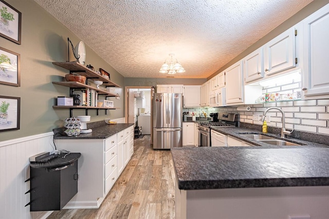 kitchen featuring kitchen peninsula, a textured ceiling, stainless steel appliances, white cabinets, and sink