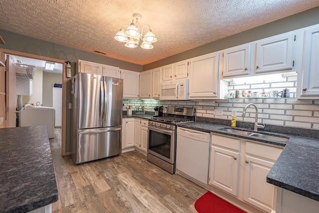 kitchen with an inviting chandelier, white cabinets, appliances with stainless steel finishes, wood-type flooring, and sink