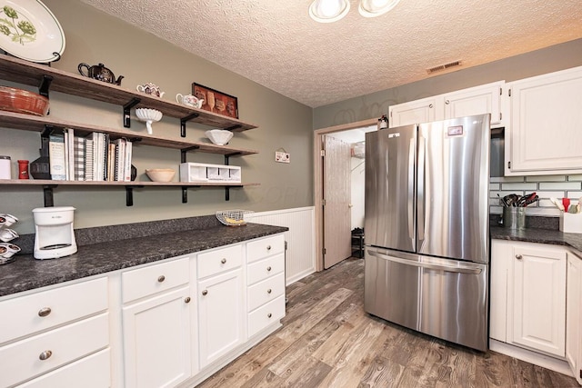 kitchen with white cabinets, a textured ceiling, light hardwood / wood-style flooring, stainless steel refrigerator, and backsplash