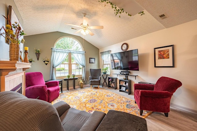 living room with a textured ceiling, a fireplace, vaulted ceiling, ceiling fan, and light hardwood / wood-style floors