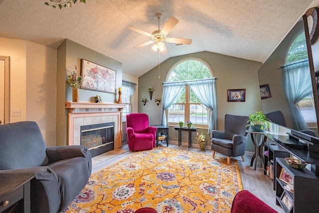 living room with a tile fireplace, ceiling fan, a textured ceiling, light hardwood / wood-style flooring, and lofted ceiling