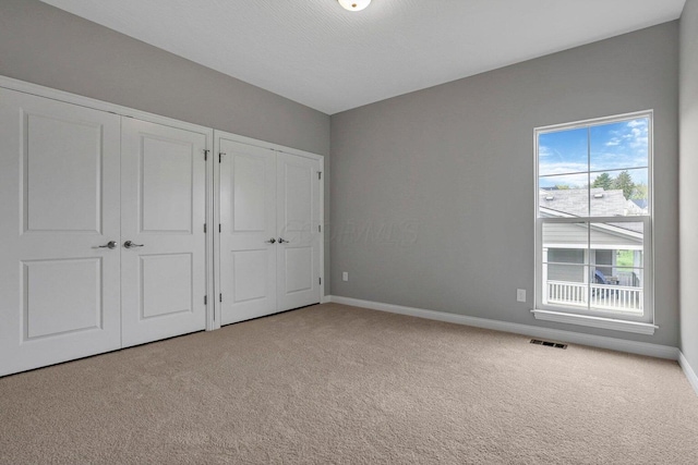 unfurnished bedroom with carpet, visible vents, baseboards, and two closets