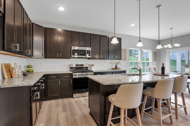 kitchen with appliances with stainless steel finishes, a sink, dark brown cabinetry, and pendant lighting