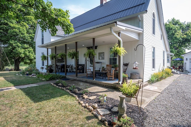 back of house featuring covered porch, a yard, a chimney, and metal roof