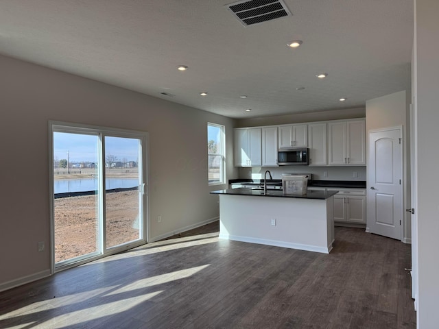 kitchen with a water view, dark hardwood / wood-style flooring, an island with sink, and white cabinets