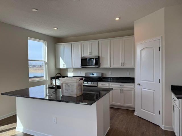 kitchen featuring dark wood-type flooring, a kitchen island with sink, dark stone countertops, stainless steel appliances, and white cabinets