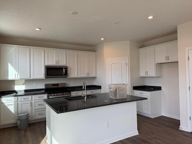 kitchen with sink, a kitchen island with sink, stainless steel appliances, dark hardwood / wood-style floors, and white cabinets