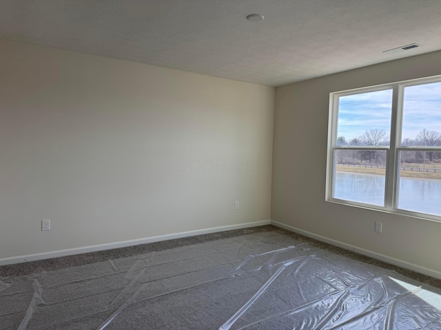 carpeted empty room featuring a water view and a textured ceiling