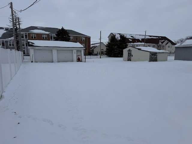 snowy yard with a garage and a storage shed