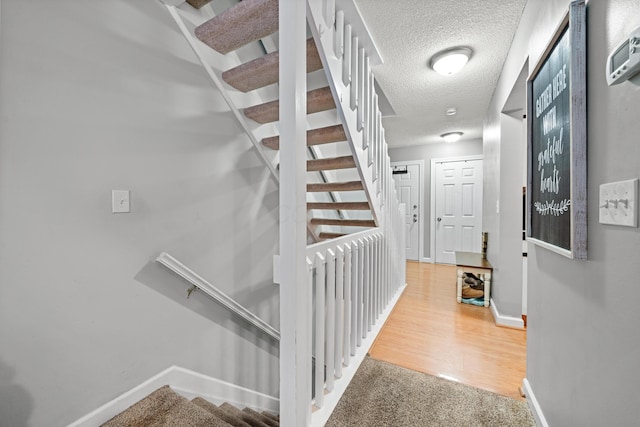 hall with baseboards, a textured ceiling, wood finished floors, and stairs