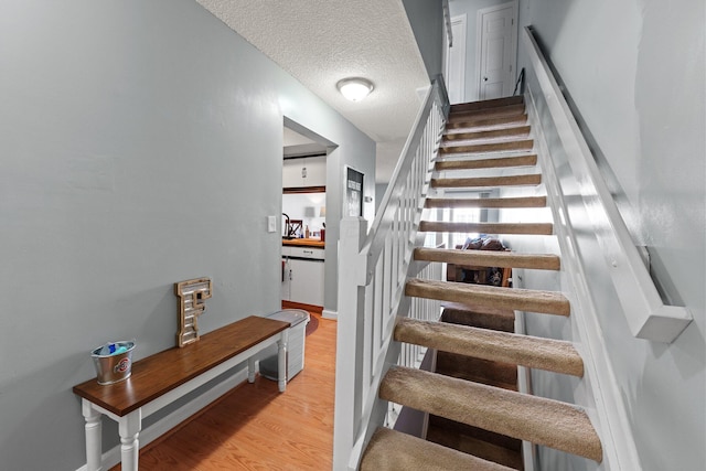 stairway with baseboards, a textured ceiling, and wood finished floors