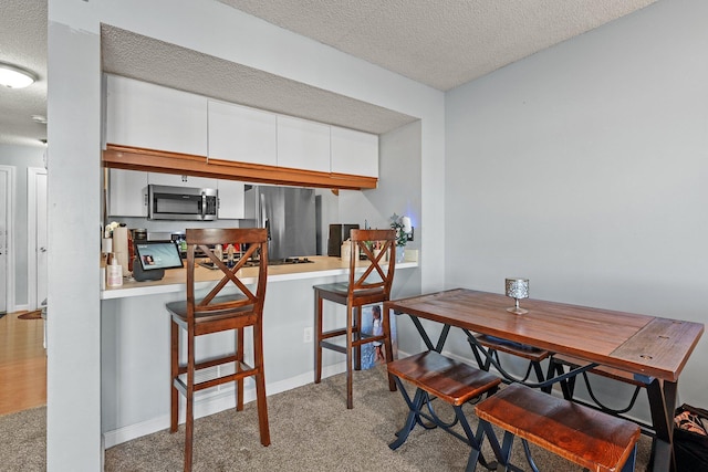 kitchen with a textured ceiling, white cabinetry, carpet floors, appliances with stainless steel finishes, and baseboards