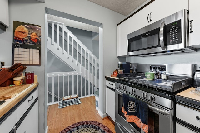 kitchen with light wood finished floors, light countertops, appliances with stainless steel finishes, a textured ceiling, and white cabinetry