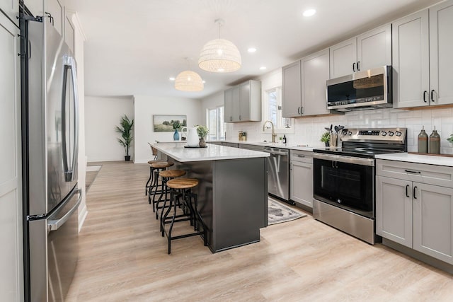 kitchen with a kitchen bar, appliances with stainless steel finishes, gray cabinetry, decorative light fixtures, and a kitchen island