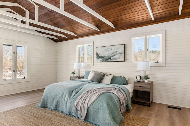 bedroom with vaulted ceiling with beams, light hardwood / wood-style flooring, wooden walls, and wooden ceiling