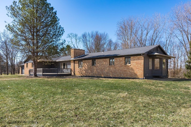 back of property featuring a yard, brick siding, a deck, and a chimney