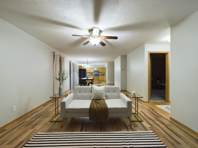 living room featuring ceiling fan, light wood-type flooring, and a textured ceiling