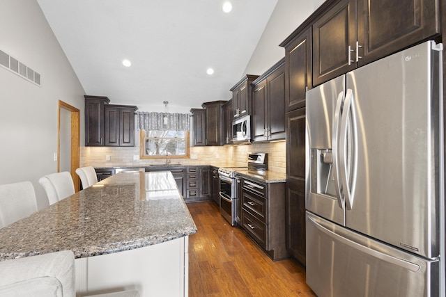 kitchen featuring a breakfast bar area, tasteful backsplash, dark stone countertops, appliances with stainless steel finishes, and a kitchen island