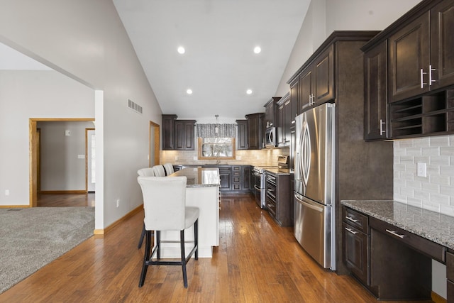 kitchen featuring dark wood-type flooring, dark brown cabinets, a kitchen island, stainless steel appliances, and light stone countertops