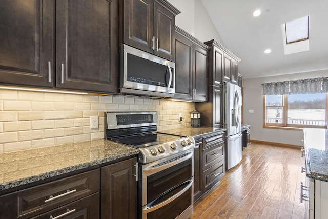 kitchen with dark wood-type flooring, appliances with stainless steel finishes, dark stone countertops, backsplash, and vaulted ceiling with skylight