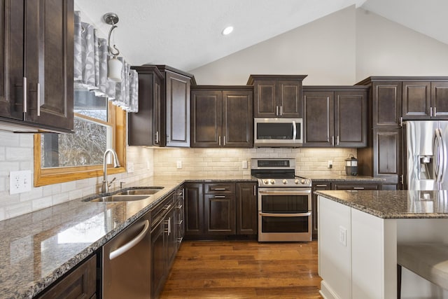 kitchen with decorative light fixtures, sink, dark stone countertops, stainless steel appliances, and dark wood-type flooring