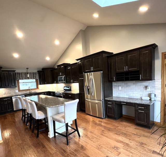 kitchen featuring a breakfast bar area, light stone counters, a center island, appliances with stainless steel finishes, and light hardwood / wood-style floors