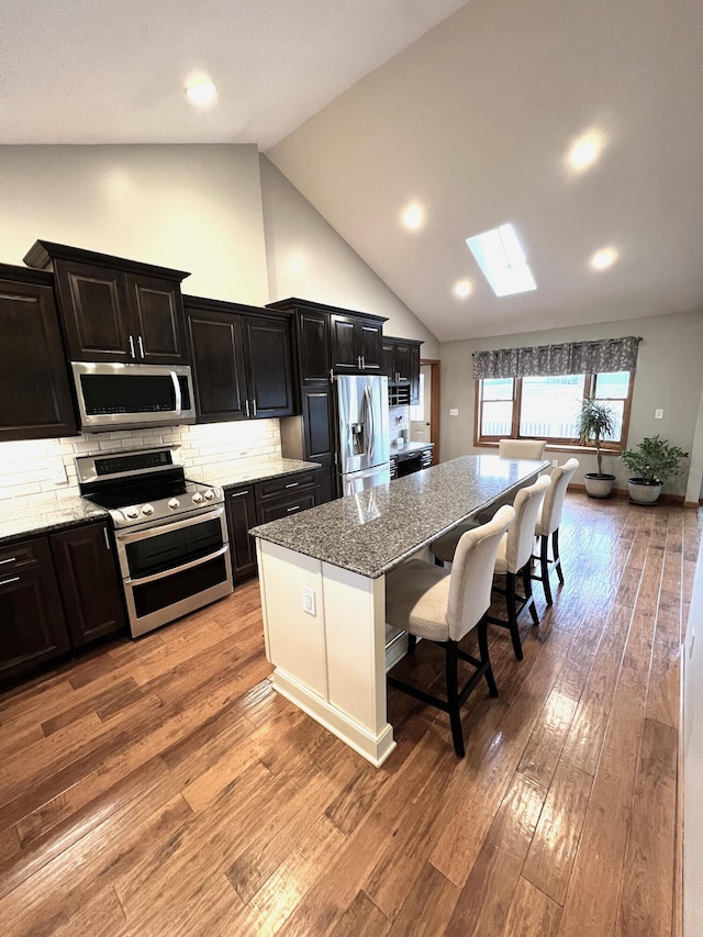 kitchen with a kitchen island, appliances with stainless steel finishes, a kitchen breakfast bar, light stone counters, and light wood-type flooring