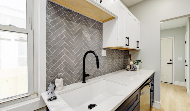 kitchen featuring sink, dishwasher, white cabinetry, light stone countertops, and decorative backsplash