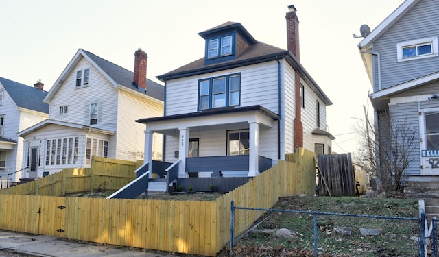 american foursquare style home with a fenced front yard, covered porch, and a chimney