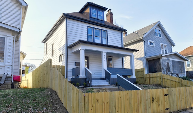 american foursquare style home featuring a porch, a fenced front yard, and a chimney