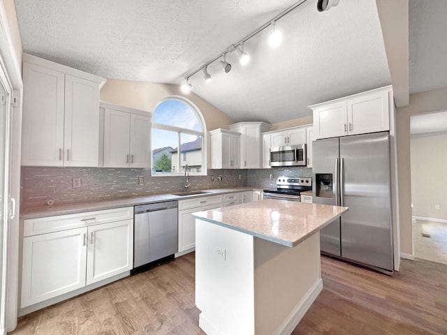 kitchen featuring vaulted ceiling, appliances with stainless steel finishes, a center island, sink, and white cabinetry