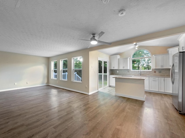 kitchen featuring stainless steel refrigerator, vaulted ceiling with beams, ceiling fan, decorative backsplash, and white cabinetry