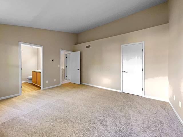 unfurnished bedroom featuring light colored carpet, vaulted ceiling, and ensuite bath