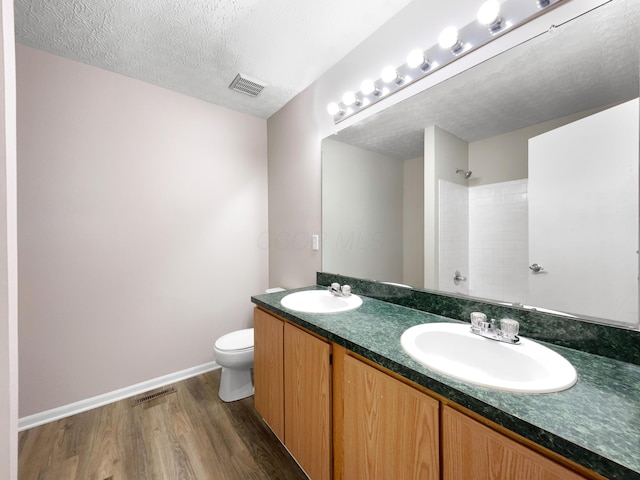 bathroom with toilet, hardwood / wood-style flooring, a textured ceiling, a shower, and vanity