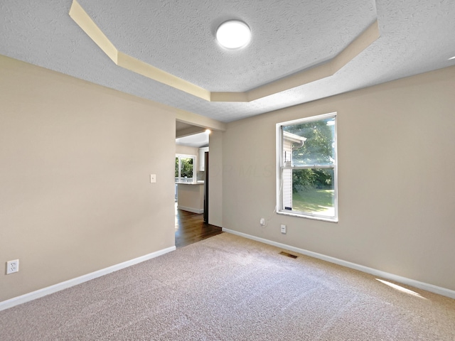 empty room with a textured ceiling, dark carpet, and a tray ceiling