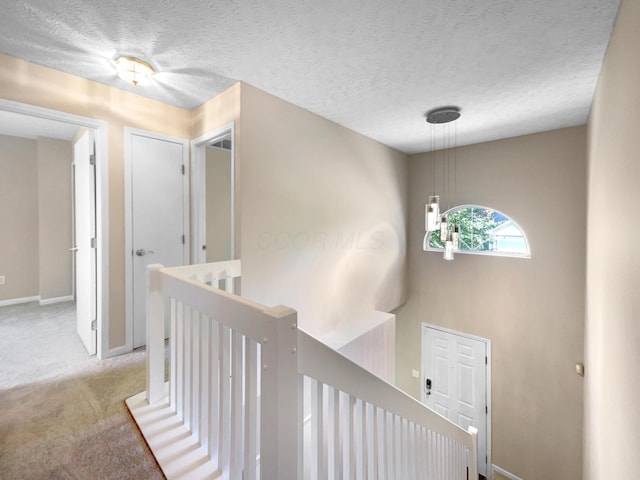 corridor with a textured ceiling and light colored carpet