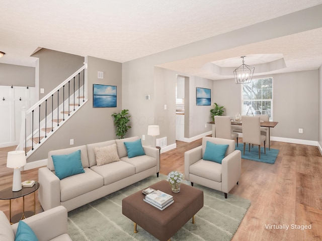 living room with hardwood / wood-style flooring, a raised ceiling, and an inviting chandelier