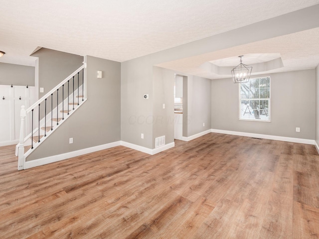 unfurnished living room featuring hardwood / wood-style flooring, a textured ceiling, a tray ceiling, and an inviting chandelier