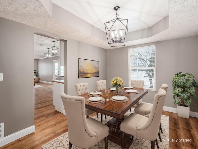 dining room with baseboards, light wood-type flooring, a raised ceiling, and a notable chandelier