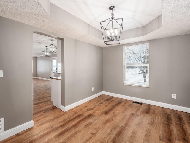 unfurnished dining area featuring a tray ceiling, wood finished floors, visible vents, and a notable chandelier