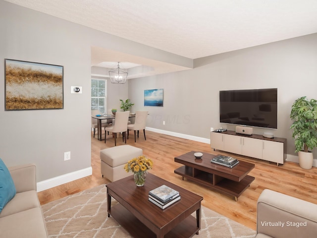 living room featuring a chandelier, a tray ceiling, baseboards, and light wood finished floors