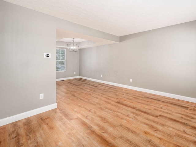 unfurnished room with light wood-type flooring, baseboards, and a notable chandelier