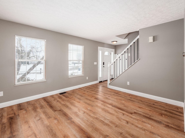 foyer entrance featuring baseboards, stairway, a textured ceiling, and wood finished floors