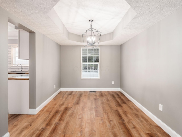 unfurnished dining area featuring a chandelier, a wealth of natural light, a raised ceiling, and baseboards