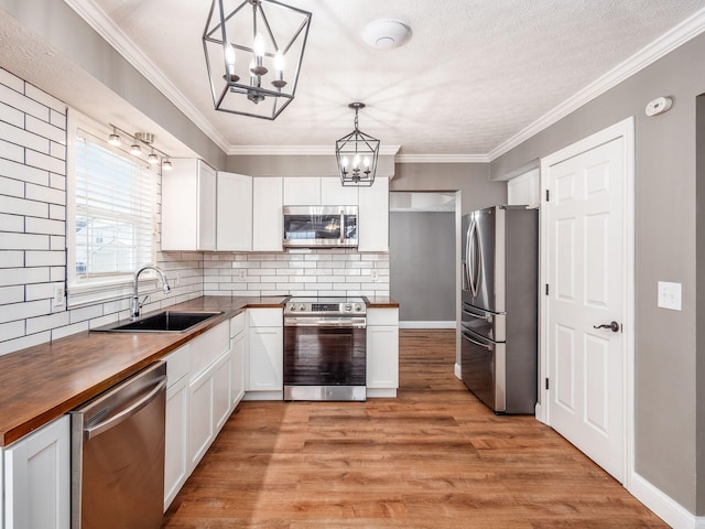 kitchen with light wood finished floors, butcher block countertops, appliances with stainless steel finishes, an inviting chandelier, and a sink