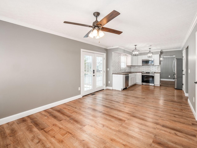 unfurnished living room with french doors, light wood finished floors, ornamental molding, a sink, and baseboards