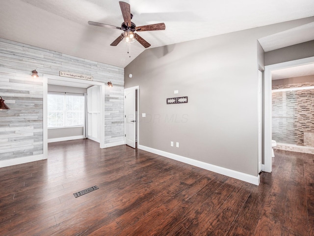 empty room with baseboards, visible vents, vaulted ceiling, and wood finished floors