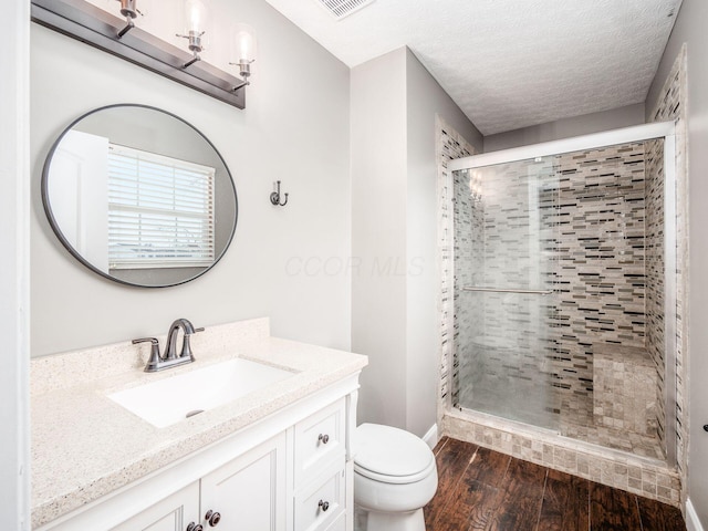 bathroom with toilet, a stall shower, vanity, a textured ceiling, and wood finished floors