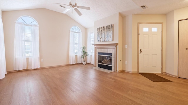 unfurnished living room with ceiling fan, a wealth of natural light, a tile fireplace, and light hardwood / wood-style flooring