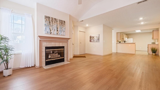 living room with light wood-type flooring, a textured ceiling, lofted ceiling, and a tile fireplace